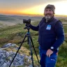 Dyn â chamera ar fynydd.
