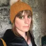 Nia Wyn Jones mewn het oren yn sefyll ger wal gerrig. 