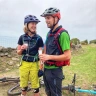 Dau feiciwr mynydd gyda gwydryn o win pefriog ym mhen draw’r llwybr.