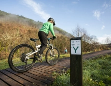 Plentyn ar gefn beic mynydd yn reidio ar hyd llwybr estyllod pren.