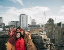 Two women and girl taking selfie on top of castle with view of modern buildings.