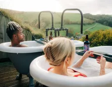two people sat side by side in individual outdoor bathtubs.