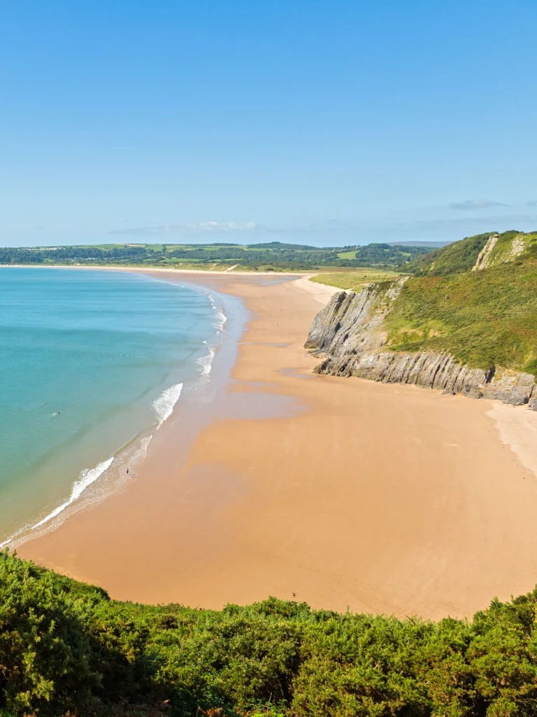 Golygfa tuag at Oxwich dros ehangder clir o ddŵr ar ddiwrnod clir llachar.