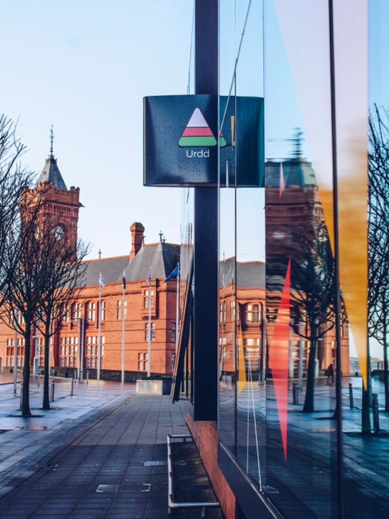 Tu allan i wersyll yr Urdd Bae Caerdydd gydag adeilad brics coch y Pierhead yn gefndir.