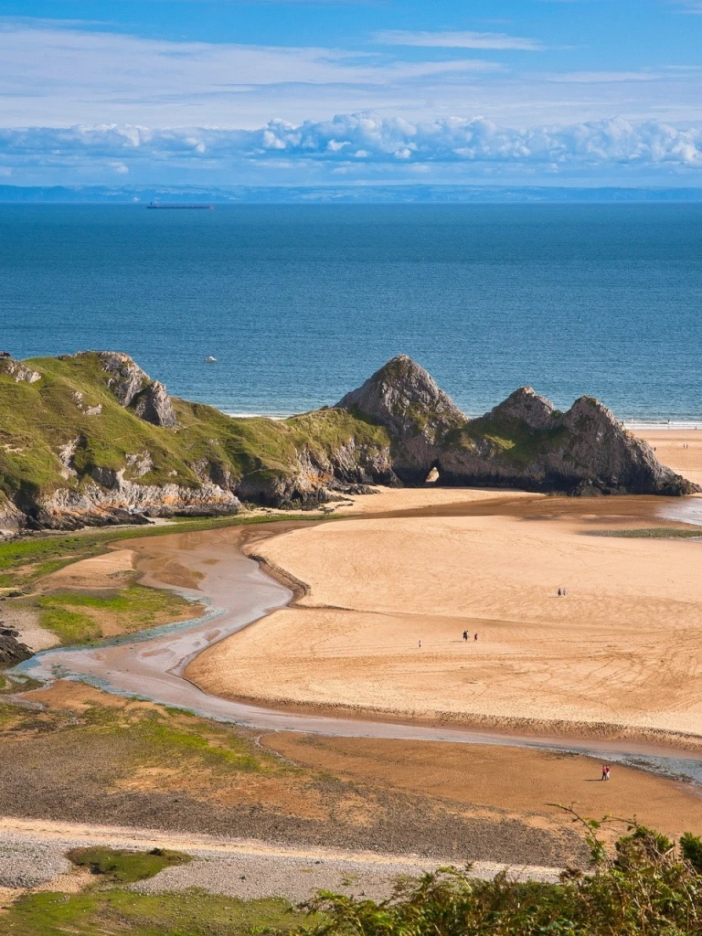 Llanw allan ym Mae'r Tri Chlogwyn gyda thraeth tywodlyd.