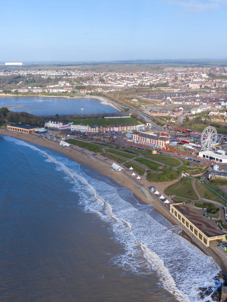 Aerial shot of a wide sandy beach with houses to the right behind of the beach and the sea to the left