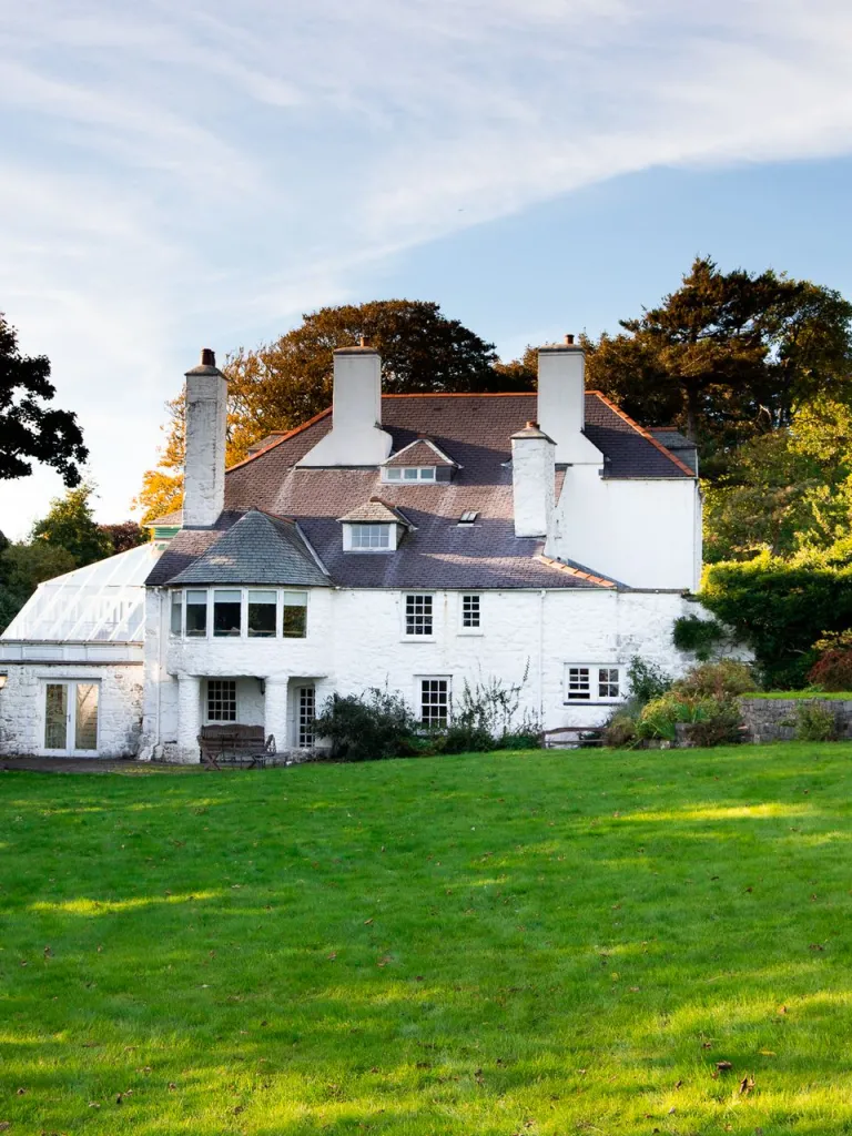 Llun o'r tu allan i dŷ mawr gwyn mewn gardd fawr
