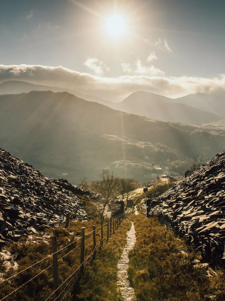 Llwybr drwy domenni gwastraff llechi mewn goleuni isel.