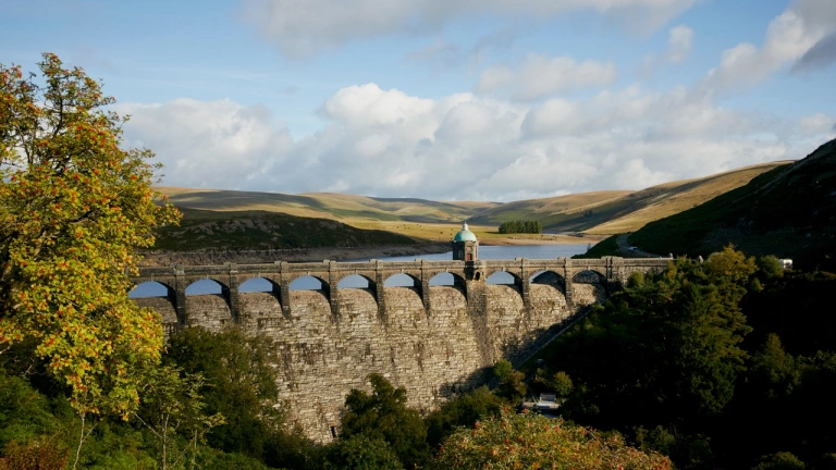 Argae sy'n dal dŵr y gronfa a bryniau amlwg yn y cefndir.