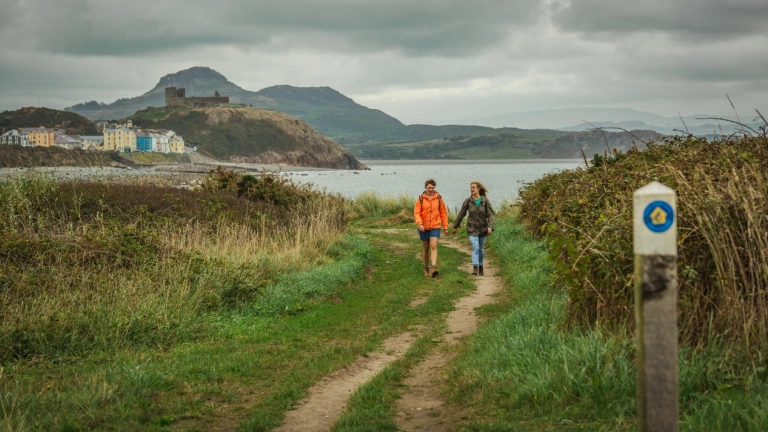 Dwy fenyw’n cerdded ar hyd Llwybr Arfordir Cymru ger Cricieth