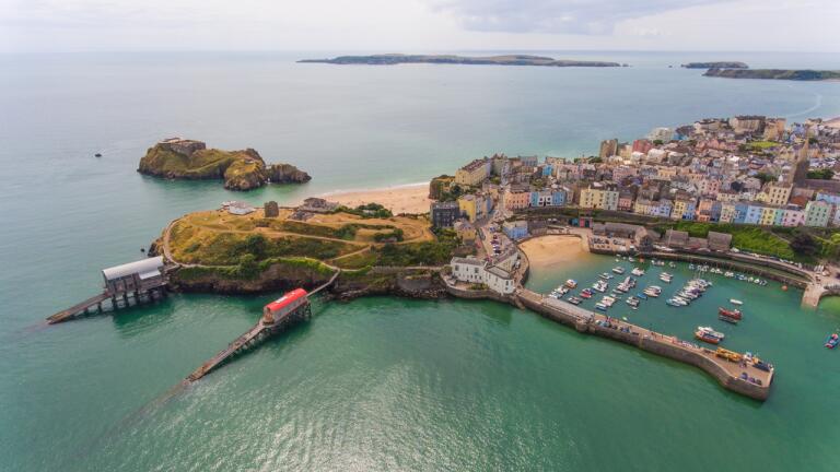 An aerial shot of a pretty harbour town with beaches, a castle, harbour and lifeboat station.