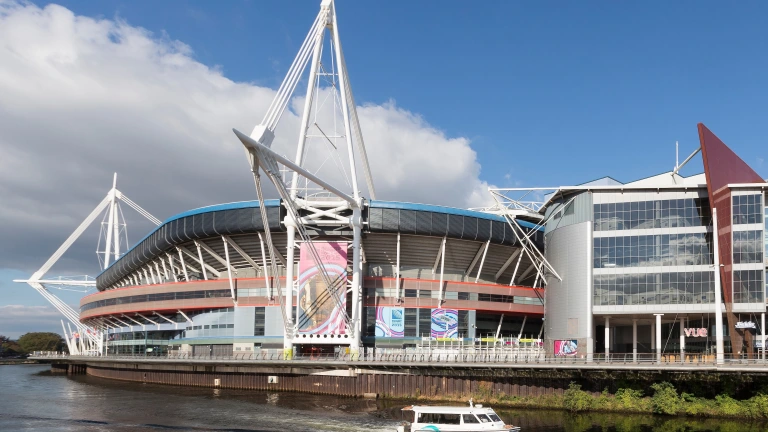 Stadiwm chwaraeon fawr ger yr afon, gyda chwch yn hwylio heibio