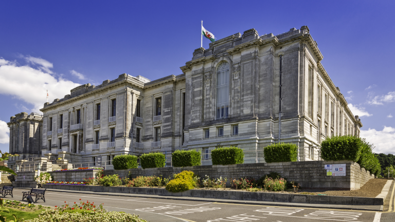 Llun o'r tu allan i Lyfrgell Genedlaethol Cymru, a baner Cymru yn hedfan uwchben.