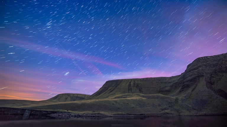 Llun o olion y sêr yn yr awyr, uwchben y llyn gyda mynyddoedd yn y cefndir