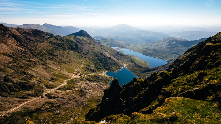 Llun ar ddiwrnod disglair gyda golygfeydd o'r Wyddfa o'r mynyddoedd a'r llynnoedd.