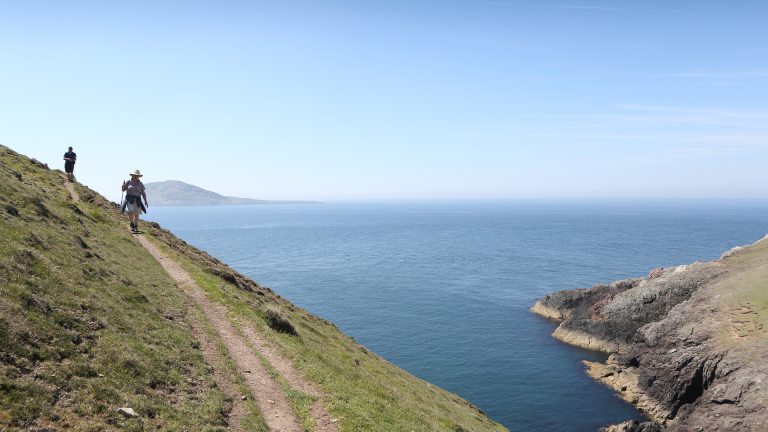 Cwpwl yn cerdded ar hyd Llwybr Arfordir Cymru gyda'r môr ar yr ochr dde