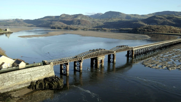Edrych i lawr ar ddau berson yn defnyddio byrddau syrffio eFoil o dan Bont Abermaw
