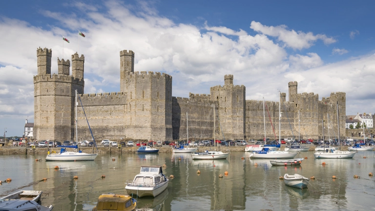 castell yn y cefndir â chychod o’i flaen