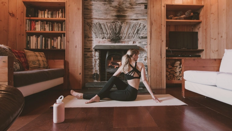 Menyw yn gwisgo cit du yn gwneud symudiad yoga o flaen y tân