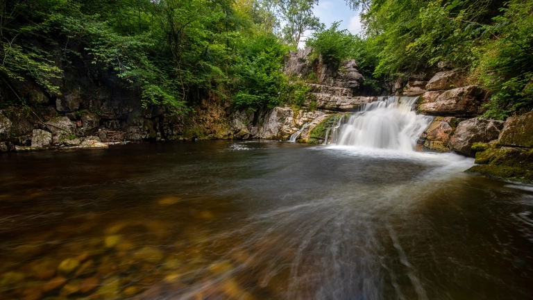 Rhaeadr dros greigiau’n llifo i bwll llydan.