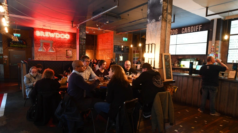 Criw o ffrindiau’n eistedd wrth fwrdd mewn bar.