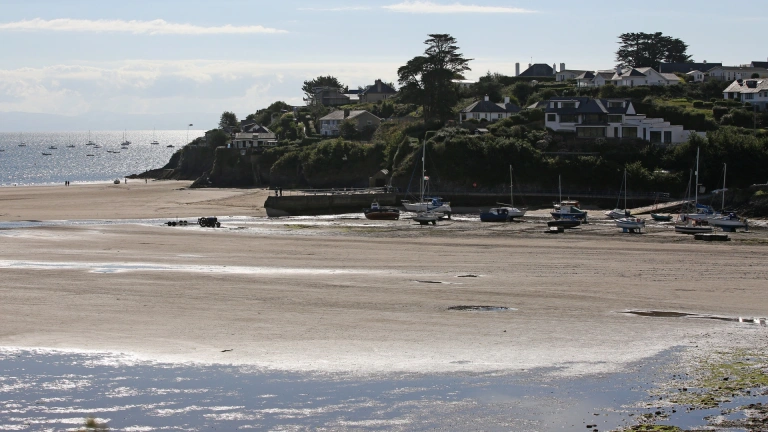 Harbwr Abersoch gyda chychod a chychod hwylio wedi'u hangori ar y traeth gyda'r llanw allan.