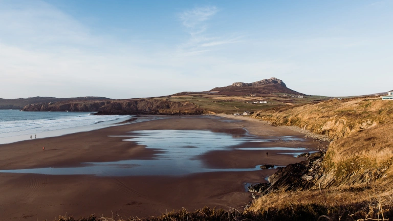 traeth gyda dŵr ar dywod a bryn.
