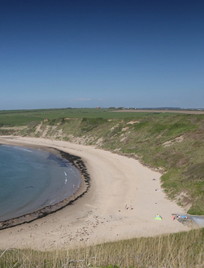 Y môr glas wrth ymyl traeth tywodlyd wedi'i amgylchynu gan fryniau gwyrdd.