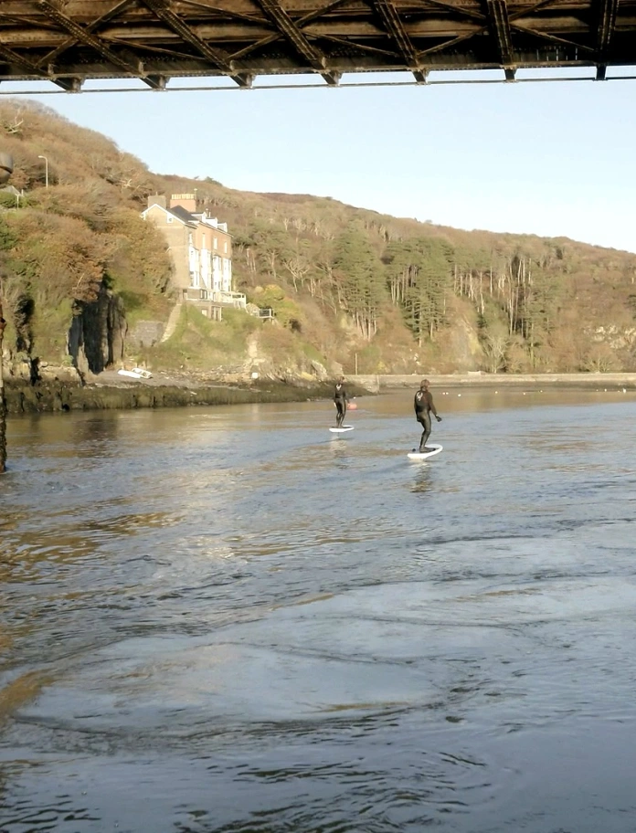 Dau berson yn defnyddio byrddau syrffio eFoil ar afon