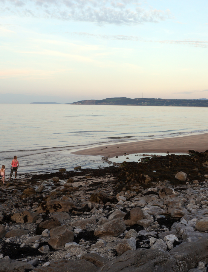 Teulu yn archwilio traeth creigiog a thywod yn y pen pellaf