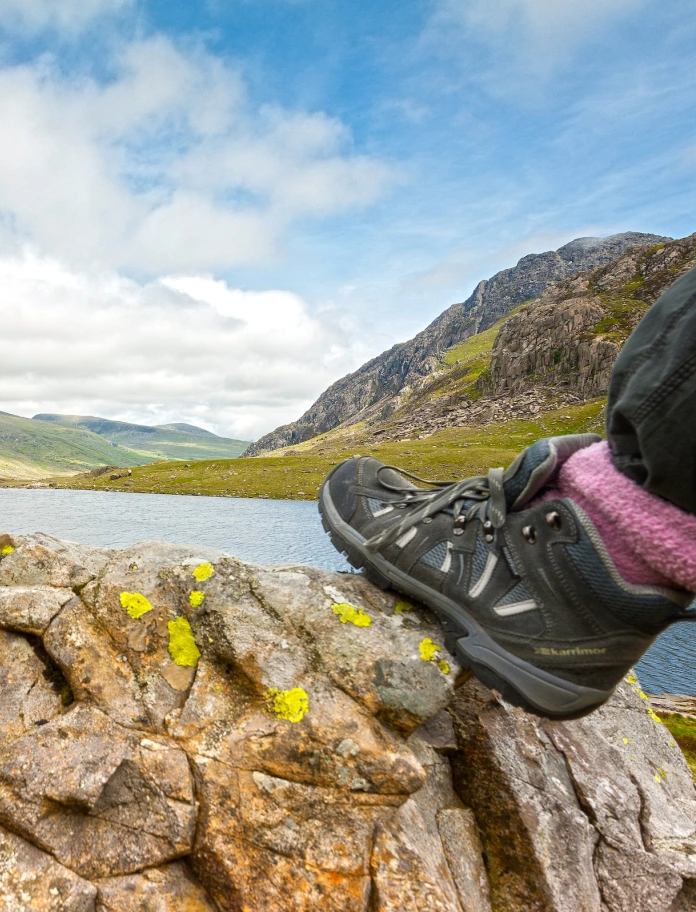 Llun o droed cerddwr ar graig o flaen Llyn Idwal