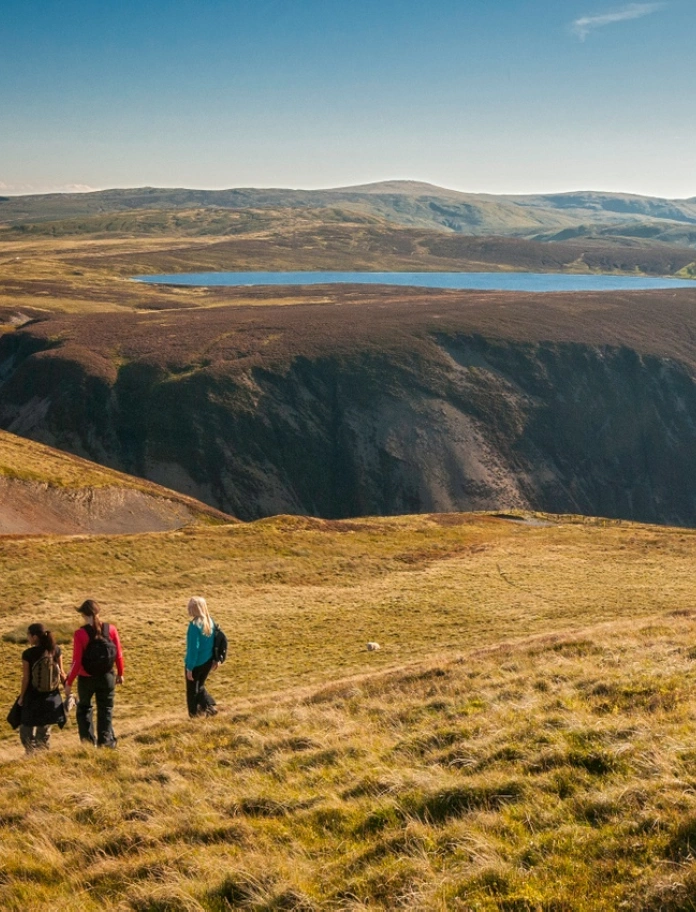 Tair dynes yn cerdded dros y mynydd gyda golygfeydd o'r mynyddoedd