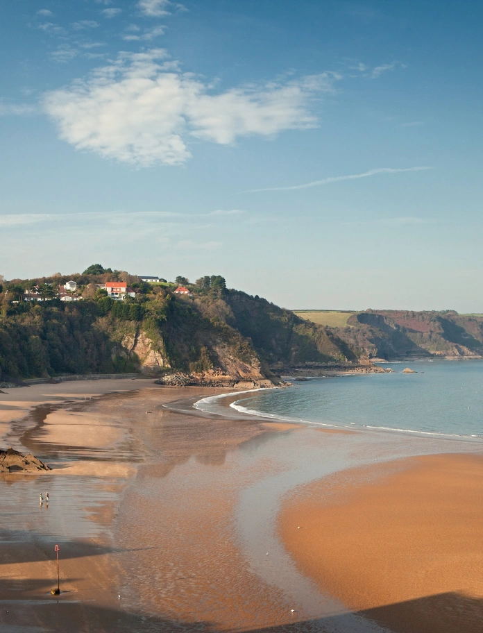 Llun o'r traeth gydag adeiladau ar y clogwyni yn y cefndir