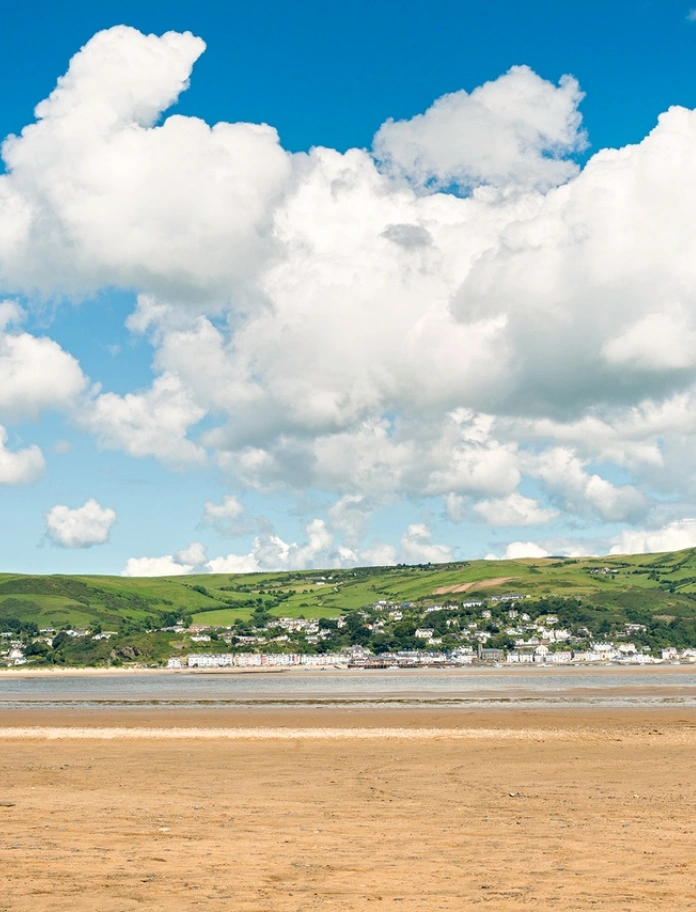 Golygfa o draeth tywodlyd ac awyr las gyda chymylau gwyn