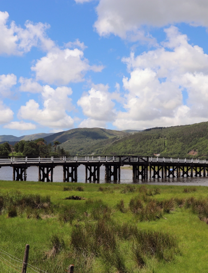 Pont bren dros afon gydag awyr las a chymylau.