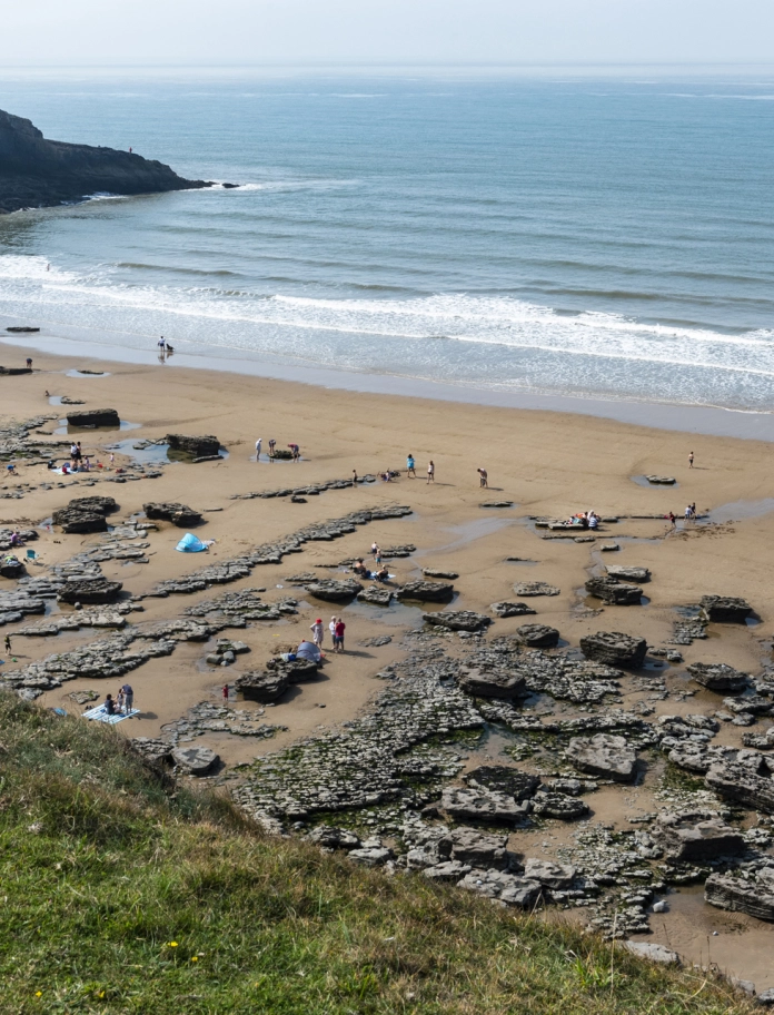 Traeth tywodlyd prysur gyda phyllau creigiau a chlogwyni.