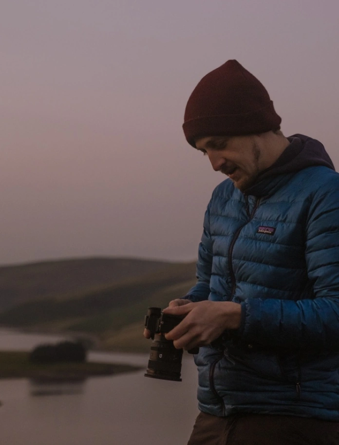 Golygfa ochr o ddyn yn yr awyr agored mewn golau isel yn edrych i lawr ar gefn camera.