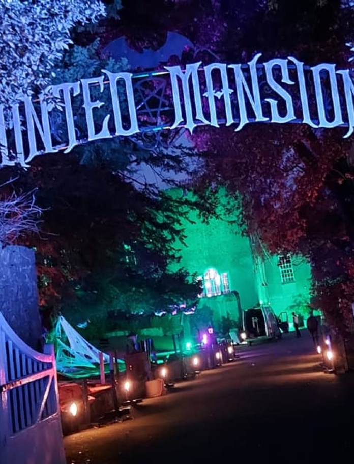 Llun gyda'r nos gyda goleuadau ac arwydd 'Haunted Mansion' uwchben giât.