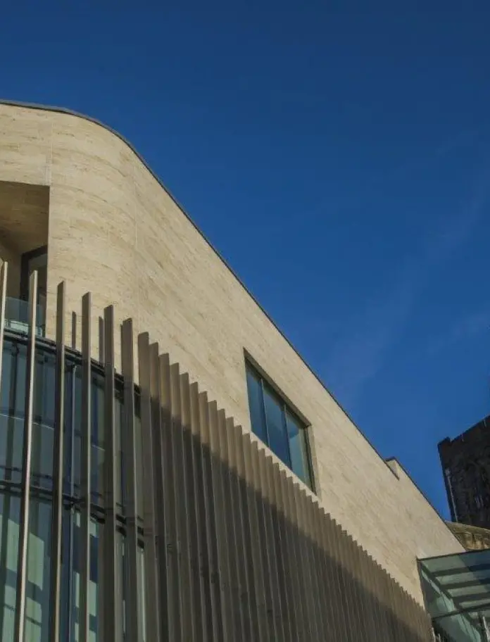 Adeilad newydd Pontio â choncrid a phaneli ffenestri gwydr mawr yn erbyn rhan hŷn twr y brifysgol