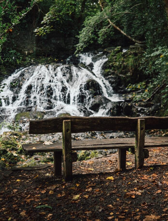 Wooden bench in front of waterfall. Mainc bren o flaen y rhaeadr.