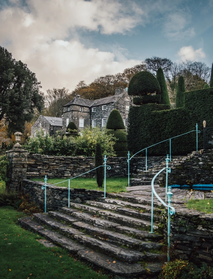 Gardd gyda grisiau, coed a thŷ yn y cefndir.