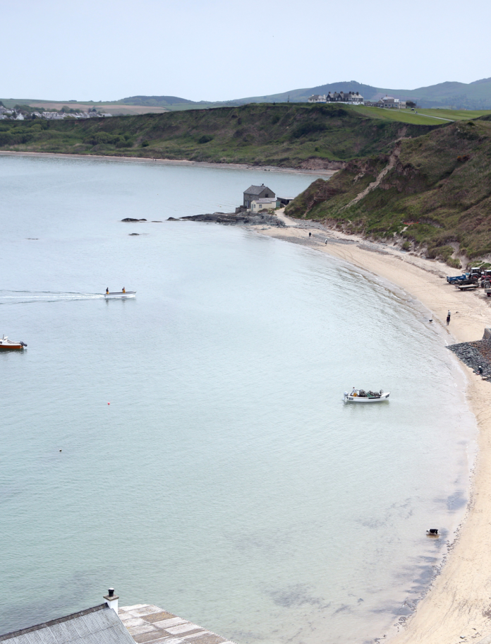Y môr wrth ymyl traeth tywodlyd gydag adeiladau a phobl.