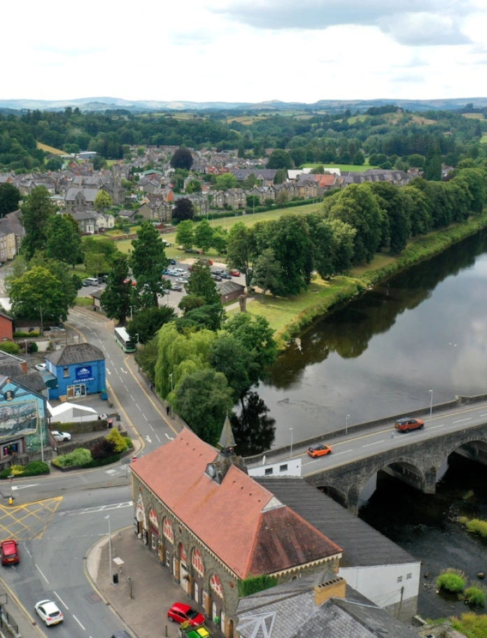 Llanfair-ym-Muallt o'r awyr. Hen bont garreg yn croesi'r afon sydd a choed gwyrdd pob ochr iddi.