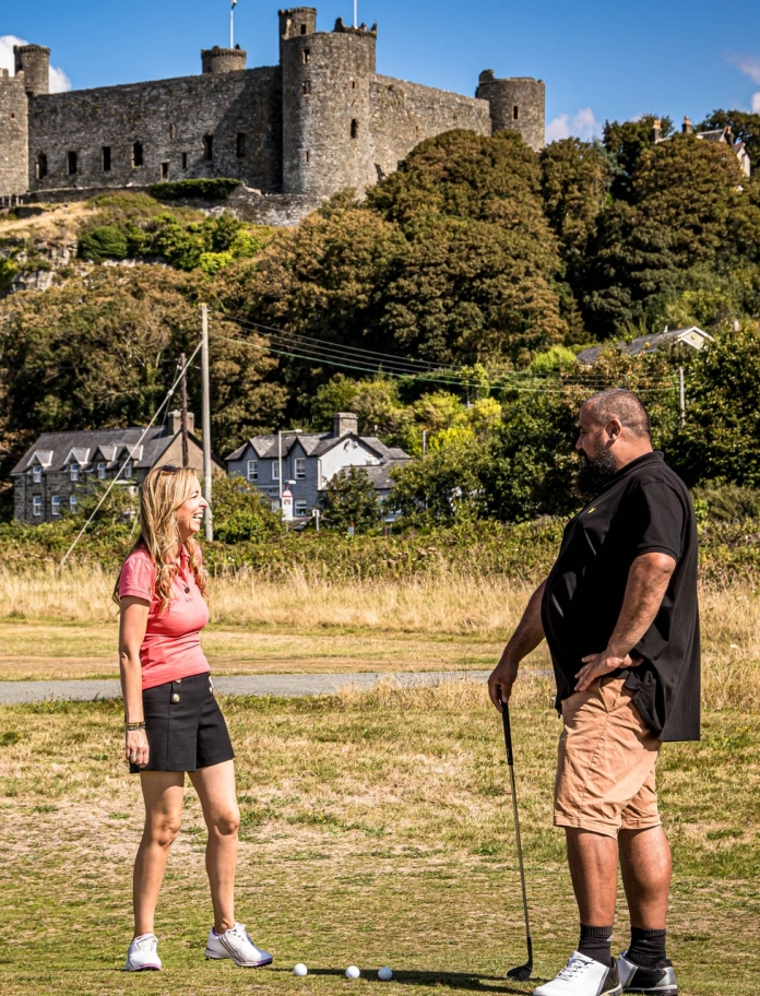 Dau golffiwr yn sgwrsio ar gwrs golff o dan gastell enfawr.