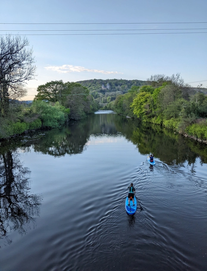 Dau berson yn padlfyrddio ar yr Afon Taf â Castell Coch yn y cefndir