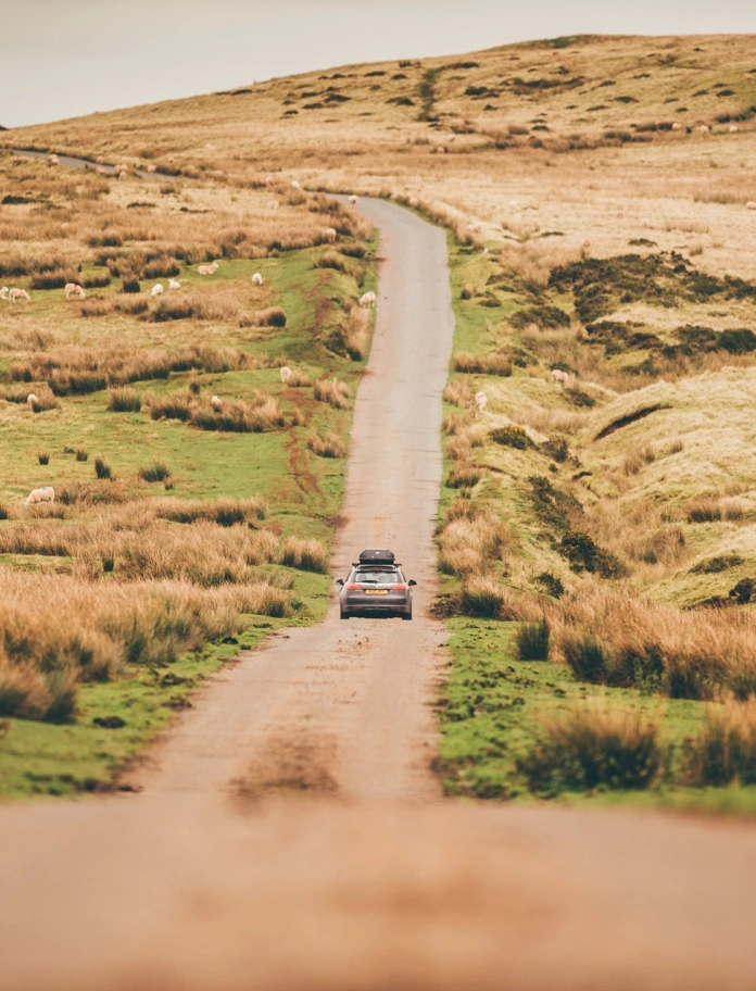 Car yn gyrru ar hyd ffordd gul anghysbell.