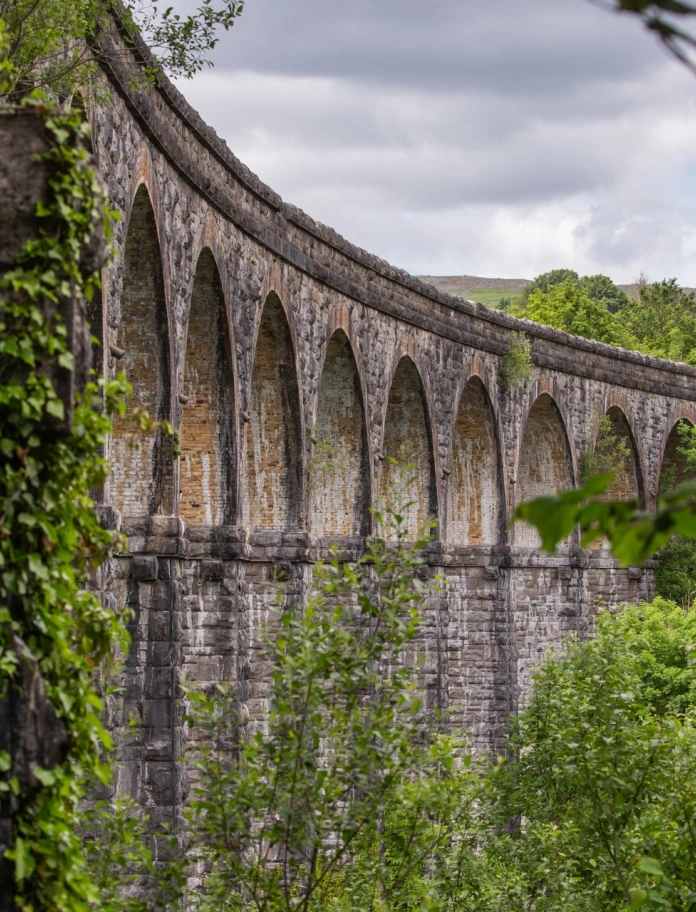 Traphont â 13 o fwâu carreg crwm, wedi’i hamgylchynu gan goed gwyrdd.