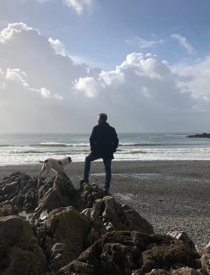Llun o ddyn a chi yn edrych allan dros Fae Pwlldu.