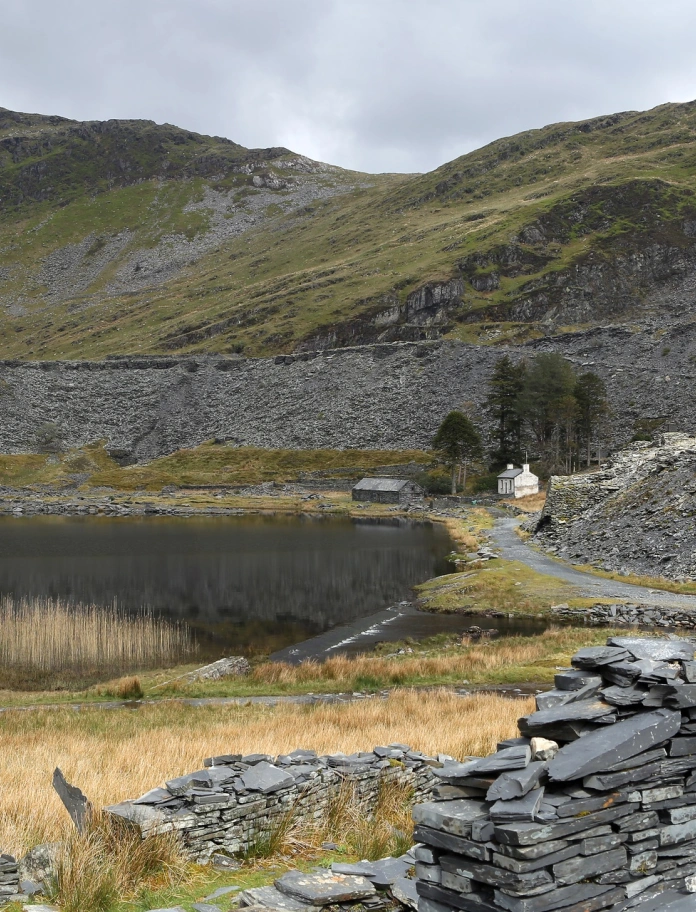 Llyn gyda mynyddoedd o'i amgylch a wal lechi. 