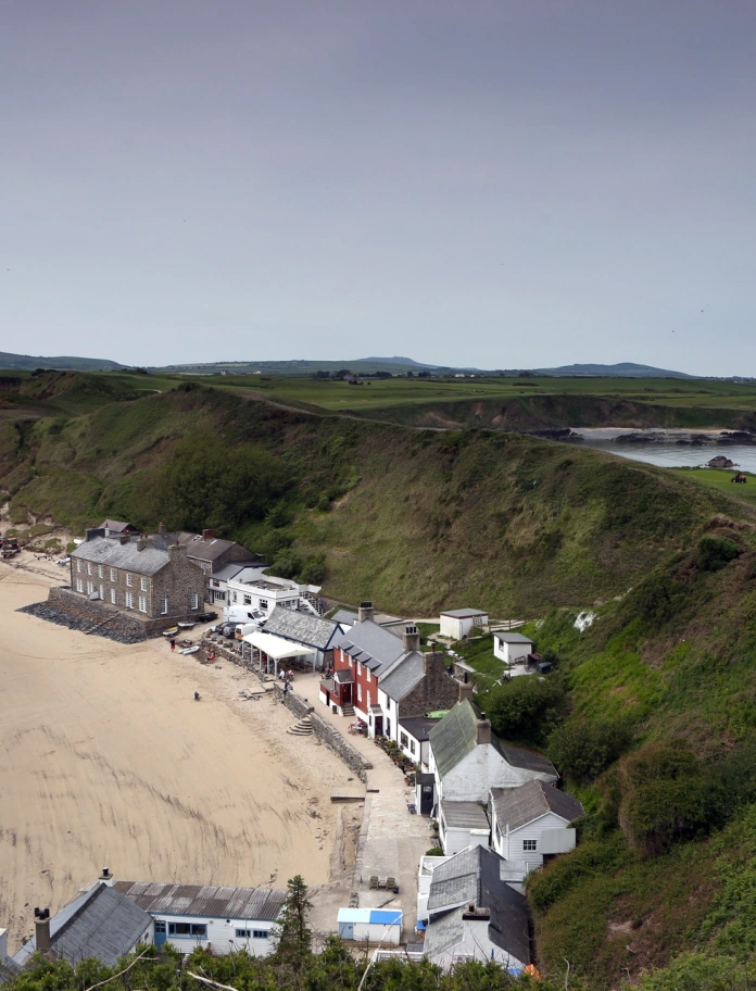 Llun o adeiladau ar y traeth, gyda bryniau gwyrdd y tu ôl.